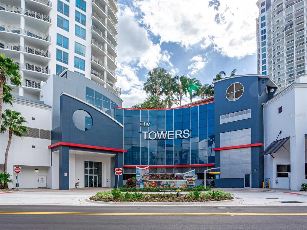 The exterior of a multi-story residential building features a blue facade with the word TOWERS — 1209 E CUMBERLAND AVENUE UNIT 2902, TAMPA, FL