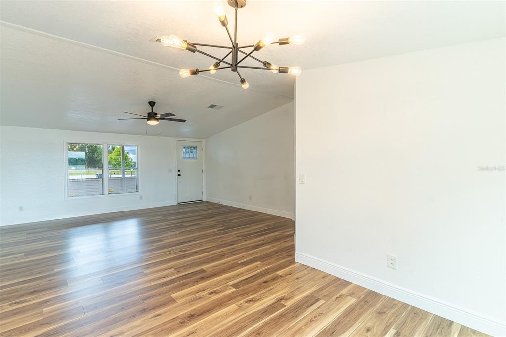 An open living area features wood-look flooring, a modern chandelier, and a ceiling fan — 8025 ALTURAS BABSON PARK CUTOFF ROAD, BARTOW, FL