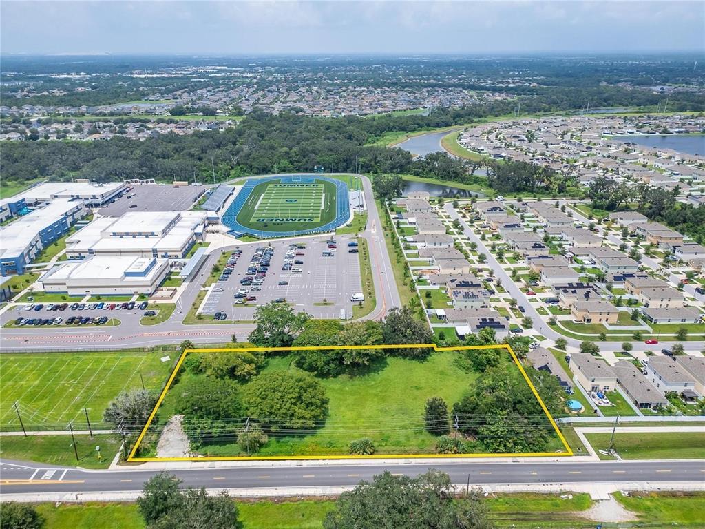 An aerial view shows a vacant, rectangular lot outlined in yellow next to a school — 10912 672 HIGHWAY, RIVERVIEW, FL