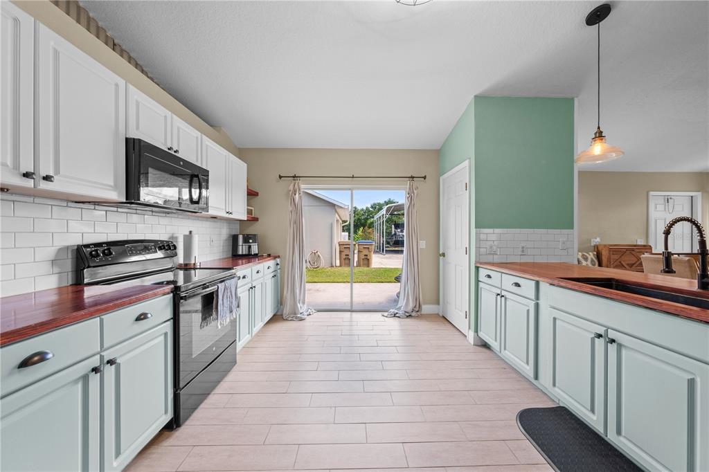 A kitchen features light blue cabinets, wood countertops, white subway tile backsplashes, and a sliding door — 4865 MEADOW DRIVE, ST CLOUD, FL