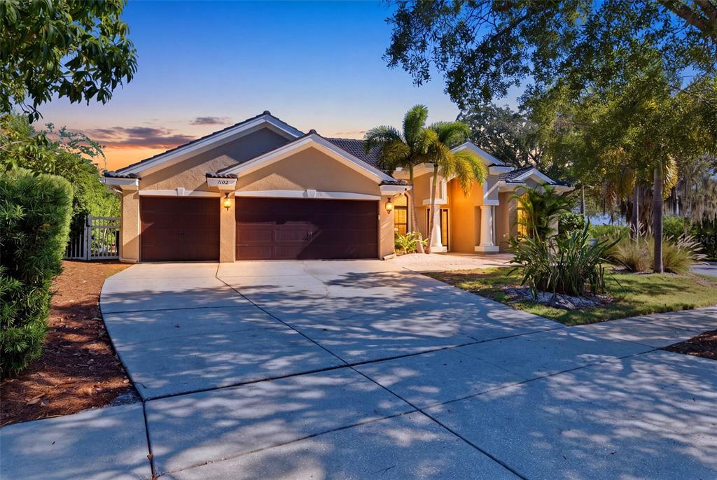 A single-story house with a three-car garage and a paved driveway at sunset — 1102 MARINA DRIVE, TARPON SPRINGS, FL