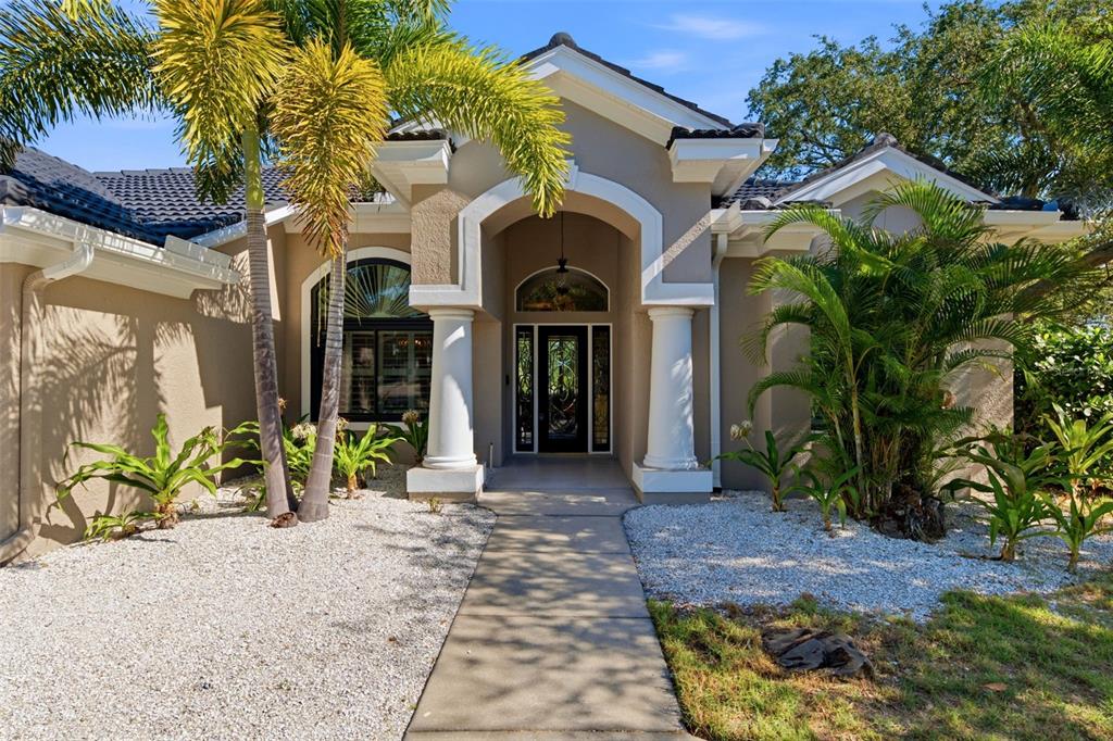 The exterior of a beige house features a covered entryway with white columns and palm trees — 1102 MARINA DRIVE, TARPON SPRINGS, FL