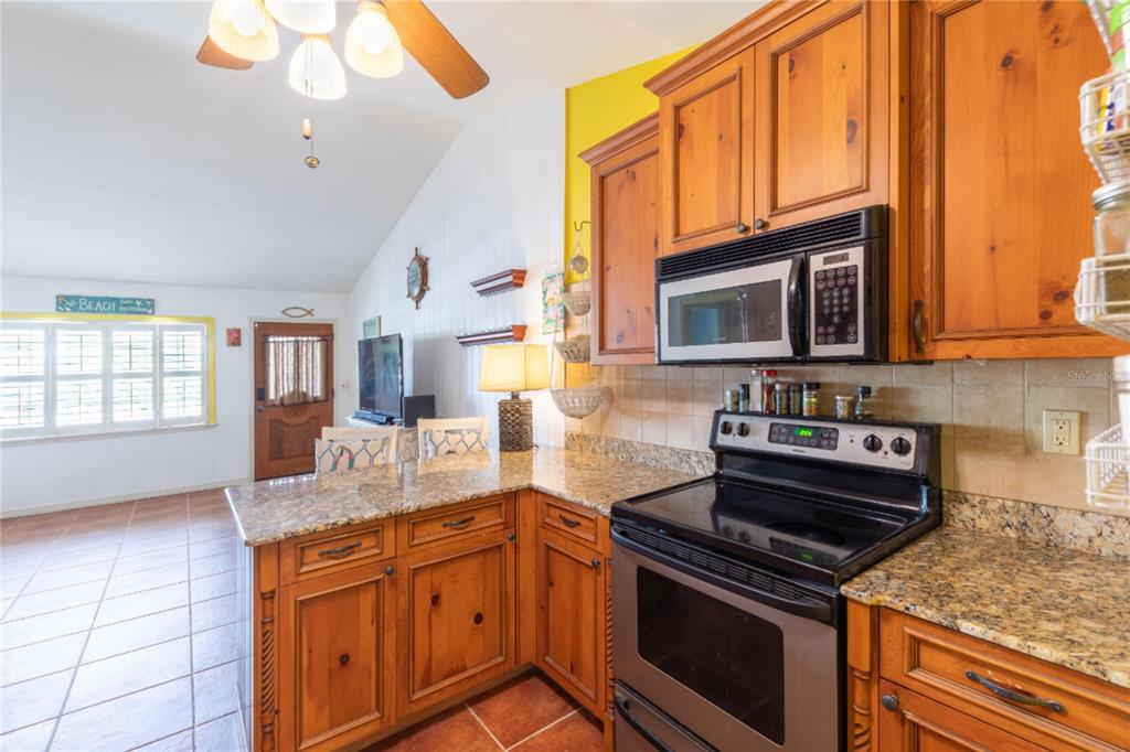 A kitchen features wood cabinets, granite countertops, and a black stove with an over-the-range microwave — 316 ALBA STREET E, VENICE, FL
