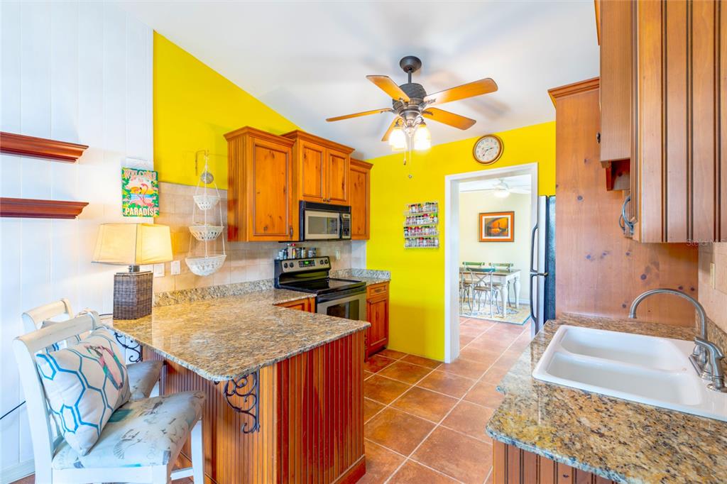 A kitchen features yellow walls, wood cabinets, granite countertops, and a ceiling fan — 316 ALBA STREET E, VENICE, FL