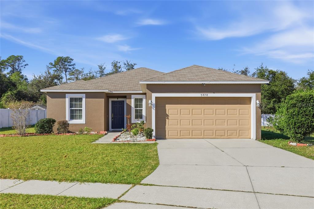 A single-story house with a tan stucco exterior, a two-car garage, and a front lawn — 7878 TANBIER DRIVE, ORLANDO, FL