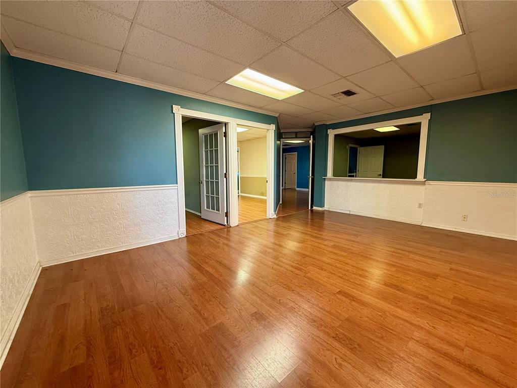 An interior room with wood-look flooring, teal walls, white wainscoting, and a drop ceiling — 7236 STATE ROAD 52 UNIT 3, HUDSON, FL