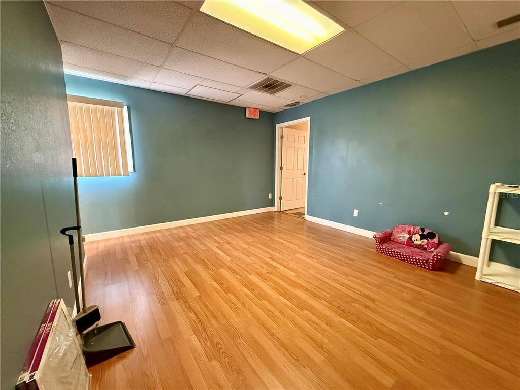 An empty room with teal walls, wood-look flooring, a drop ceiling, and a small child's sofa — 7236 STATE ROAD 52 UNIT 3, HUDSON, FL