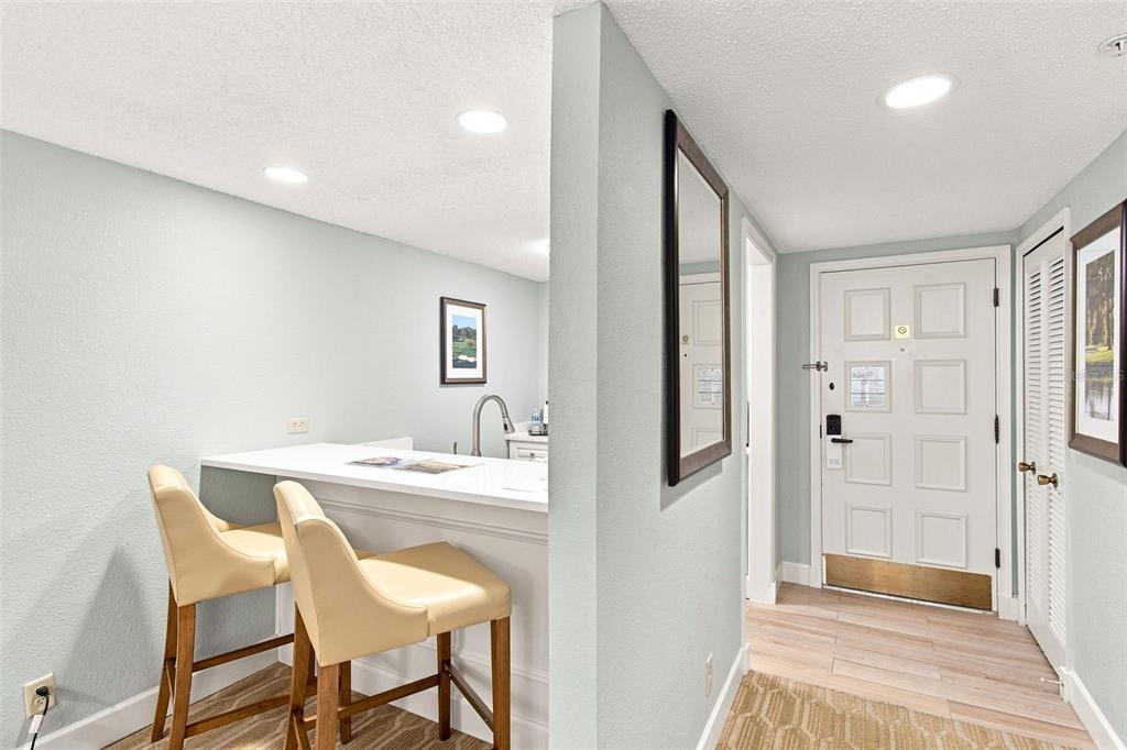 A wet bar with two stools sits adjacent to an entryway featuring a white door — 36750 US HIGHWAY 19 N UNIT 16204, PALM HARBOR, FL