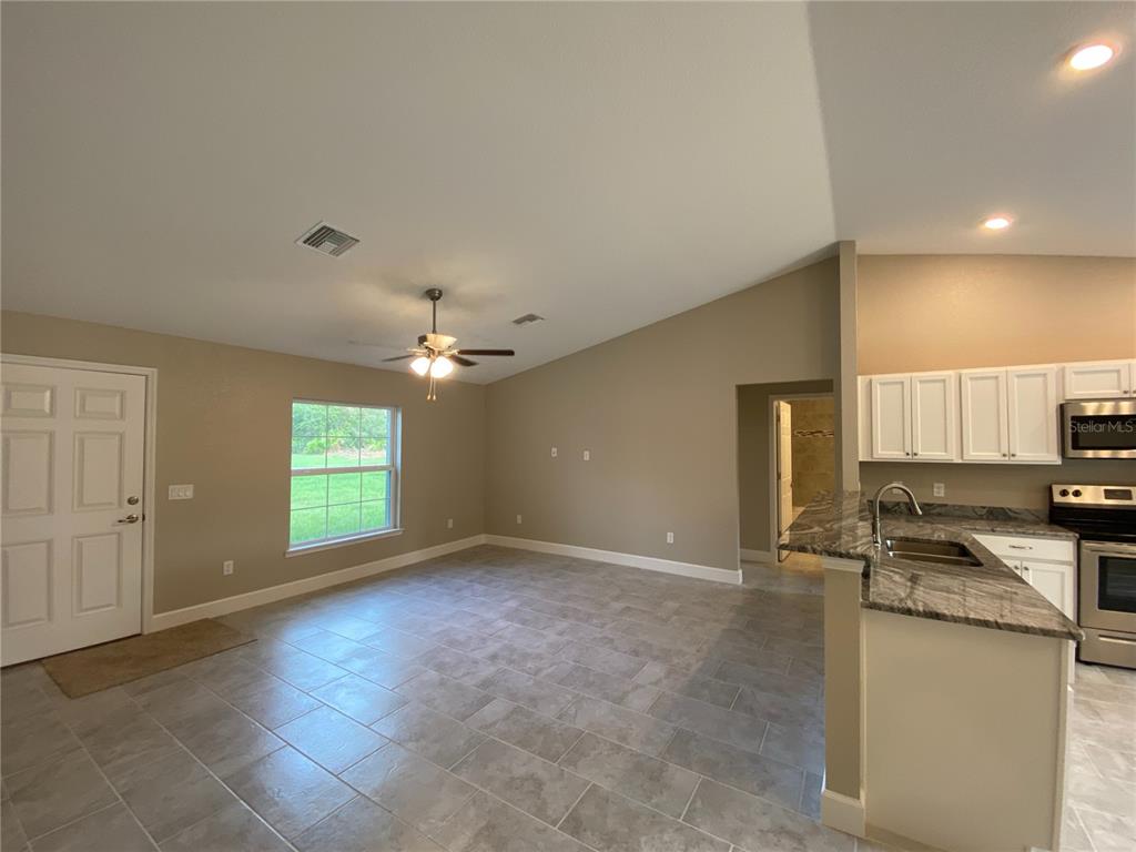 An open-concept living area features tile flooring, a vaulted ceiling, and an adjacent kitchen — 3011 SW 140TH LOOP, OCALA, FL