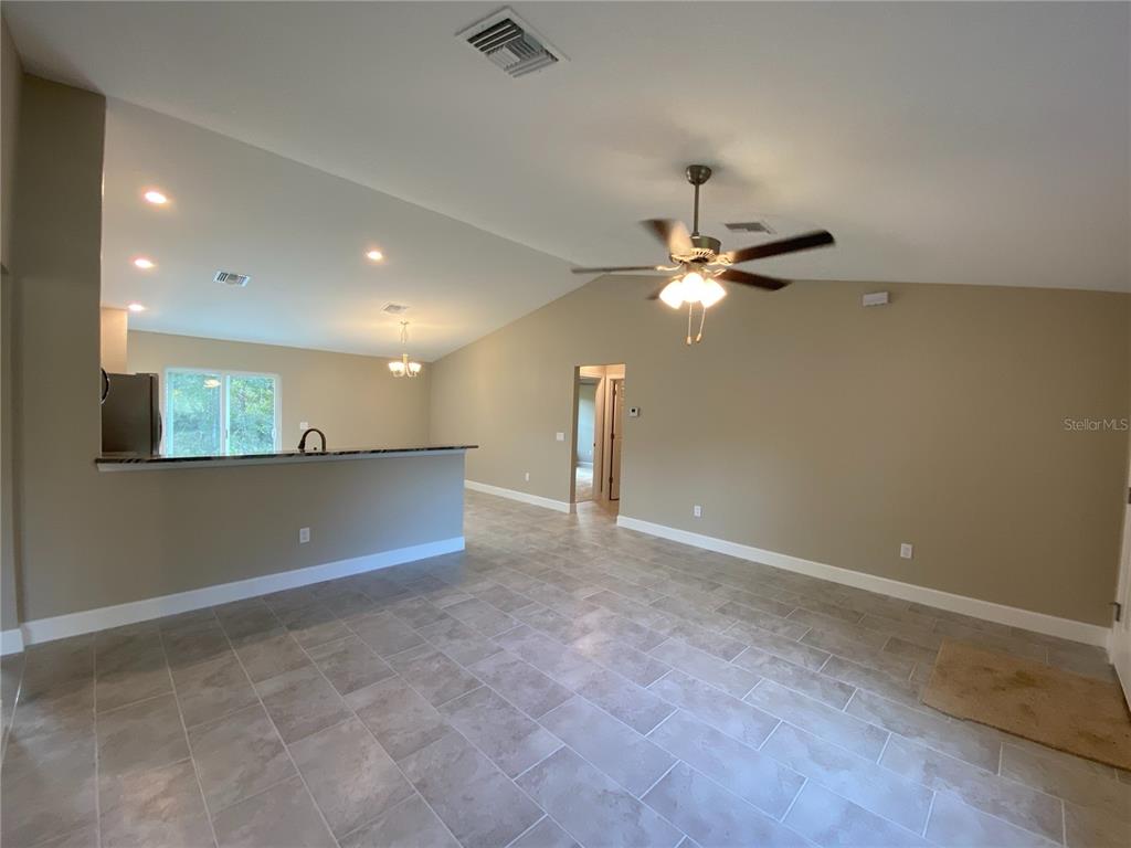 A spacious living area with tile flooring, a vaulted ceiling, and an open kitchen counter — 3011 SW 140TH LOOP, OCALA, FL