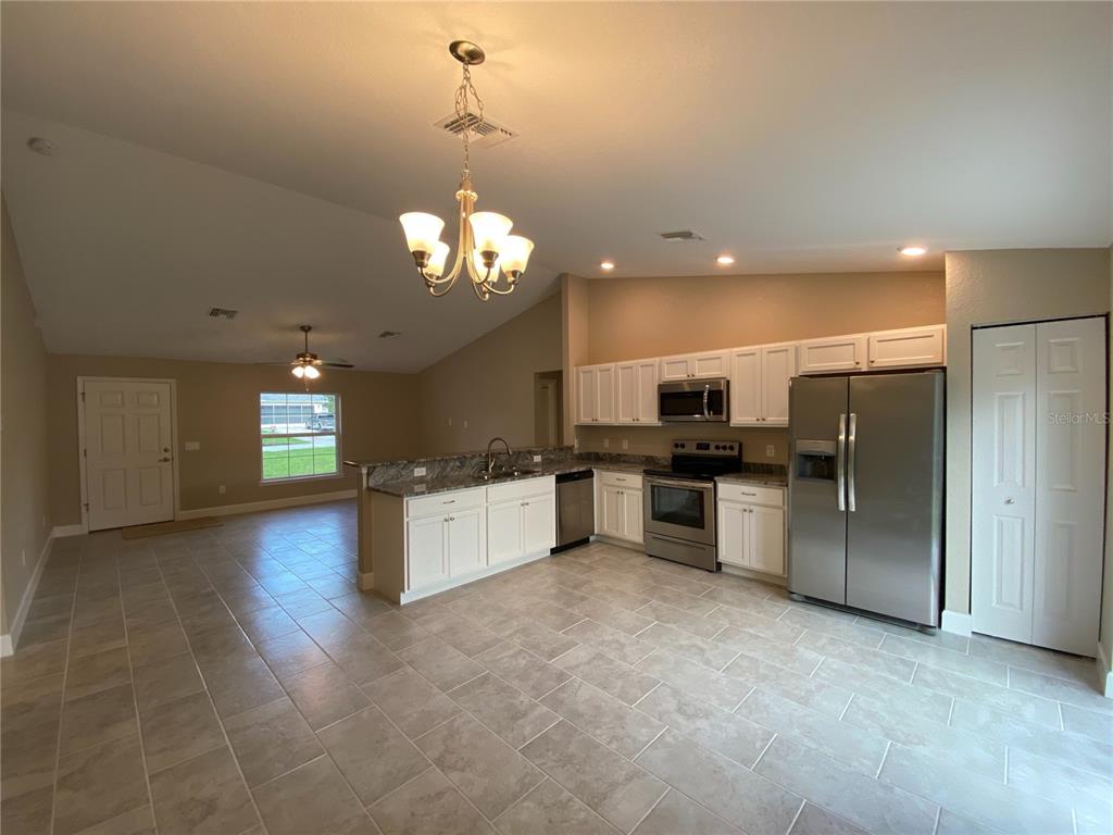 A kitchen with white cabinets, stainless steel appliances, and tile flooring opens to a living area — 3011 SW 140TH LOOP, OCALA, FL