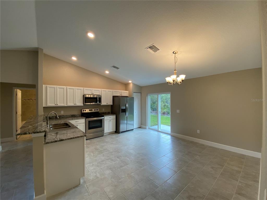 A kitchen with white cabinets, stainless steel appliances, and tile flooring opens to a dining area — 3011 SW 140TH LOOP, OCALA, FL