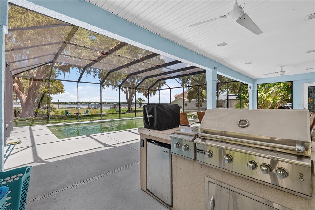 Two teal Adirondack chairs sit on a stone patio with a fire pit overlooking water — 10639 SE SUNSET HARBOR ROAD, SUMMERFIELD, FL