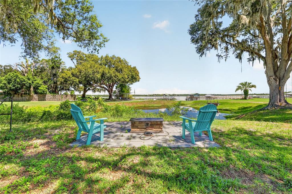 An asphalt driveway leads through an open metal gate flanked by concrete pillars and trees — 10639 SE SUNSET HARBOR ROAD, SUMMERFIELD, FL