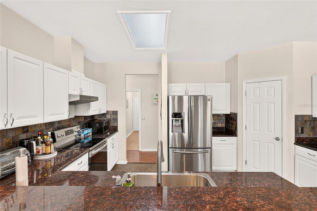 A kitchen features white cabinets, dark granite countertops, stainless steel appliances, and a tiled backsplash — 8391 SW 75TH ROAD, GAINESVILLE, FL