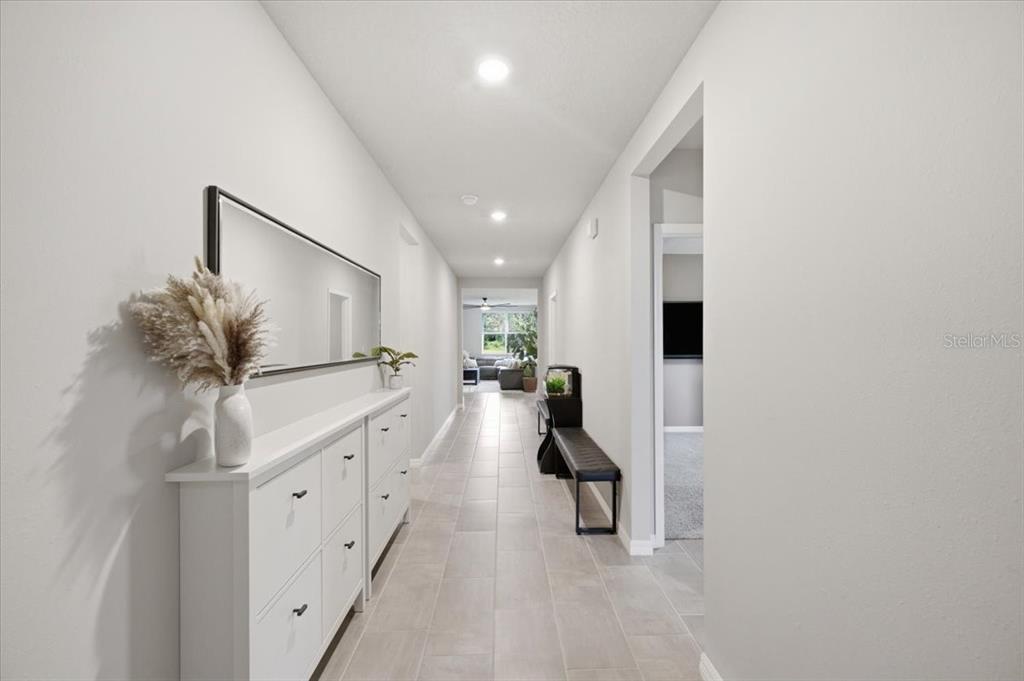 A long, white-walled hallway features light-colored tile flooring, a white storage cabinet, and a mirror — 10119 DAYBREAK GLEN, PARRISH, FL