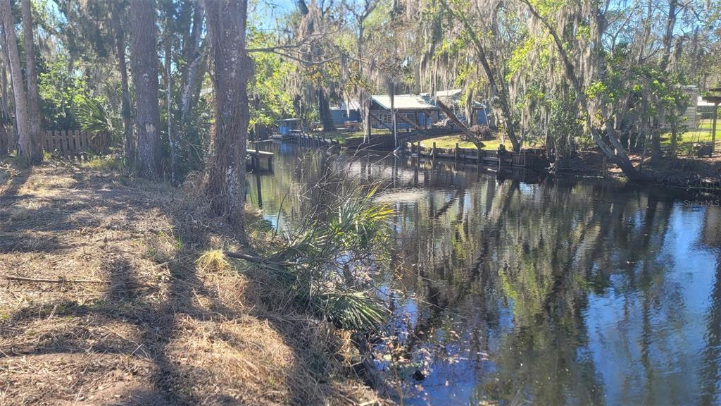 A canal flows past a wooded shoreline with a house visible in the background — 55813 SAM STREET, ASTOR, FL