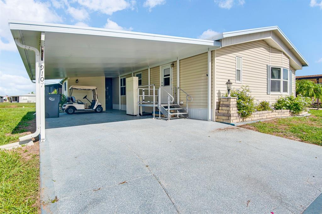 A beige manufactured home features a large carport, a concrete driveway, and metal entry stairs — 9107 34TH AVENUE E, PALMETTO, FL