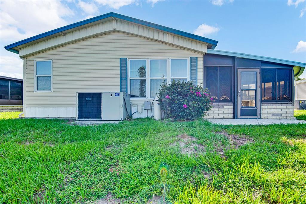 A beige manufactured home exterior features a screened-in porch, an HVAC unit, and green grass — 9107 34TH AVENUE E, PALMETTO, FL