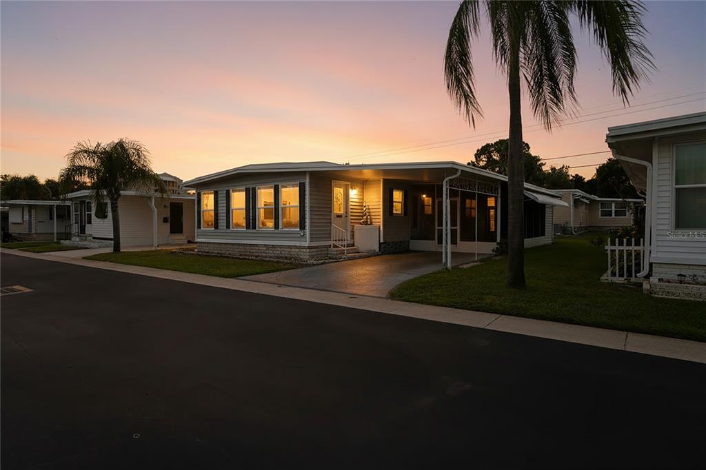 A light-colored mobile home with a carport and palm trees at sunset — 2000 E BAY DRIVE UNIT 25, LARGO, FL