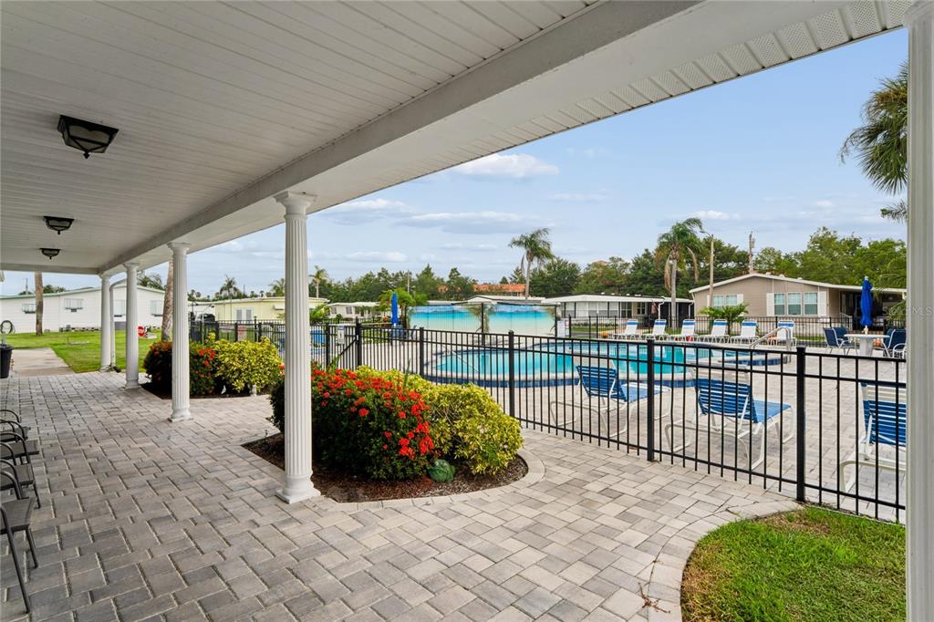 A covered patio with paver flooring overlooks a fenced swimming pool and surrounding mobile homes — 2000 E BAY DRIVE UNIT 25, LARGO, FL