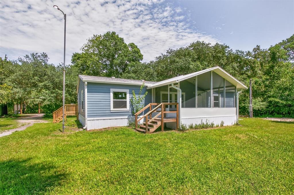 A blue mobile home features a screened-in porch, wooden stairs, and a surrounding grassy yard — 6593 CROOKED CREEK LANE, ST AUGUSTINE, FL
