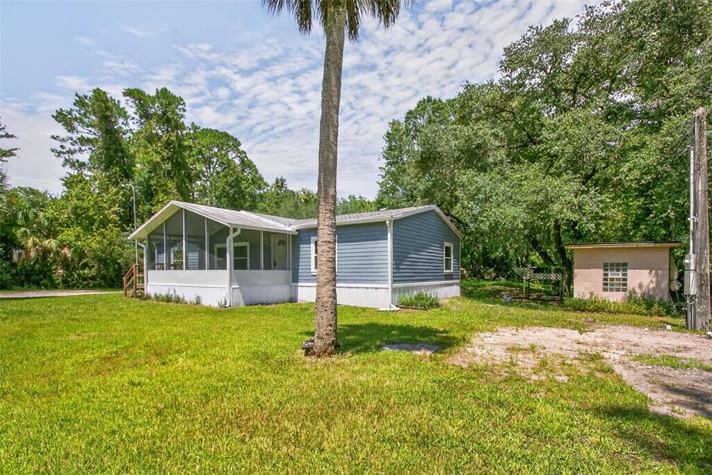 A blue mobile home with a screened-in porch sits on a grassy lot with trees — 6593 CROOKED CREEK LANE, ST AUGUSTINE, FL