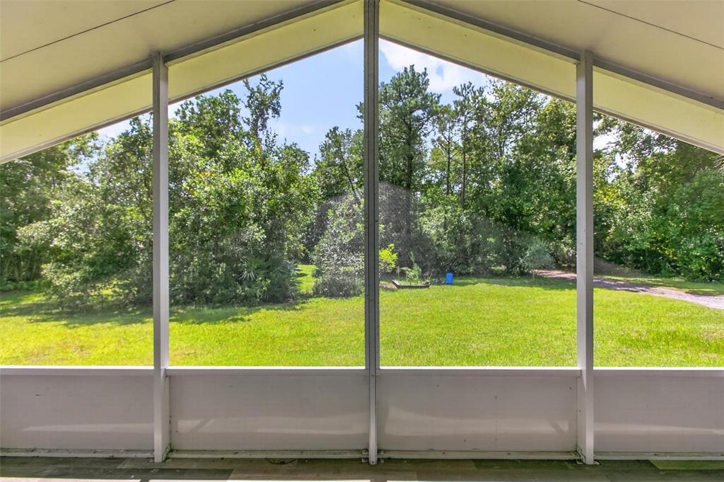 A view of a grassy yard and trees from inside a screened-in porch — 6593 CROOKED CREEK LANE, ST AUGUSTINE, FL