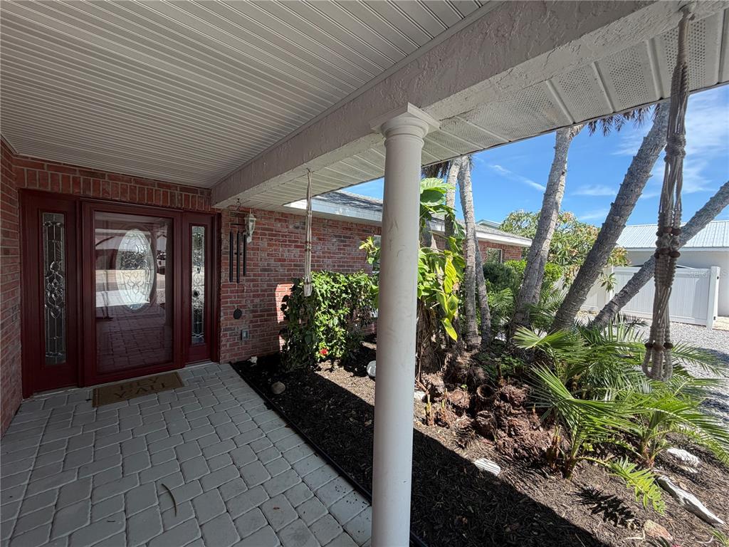 A covered brick porch features a red front door, a white column, and landscaping — 6512 KING PALM WAY, APOLLO BEACH, FL