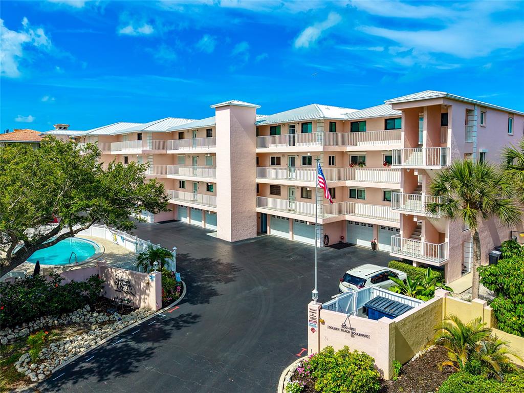 An exterior view of a multi-story pink apartment building with a swimming pool and parking — 910 GOLDEN BEACH BOULEVARD UNIT 202, VENICE, FL