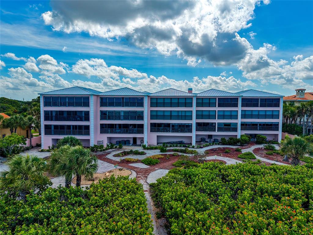 A three-story pink apartment building stands behind a landscaped courtyard with palm trees — 910 GOLDEN BEACH BOULEVARD UNIT 202, VENICE, FL