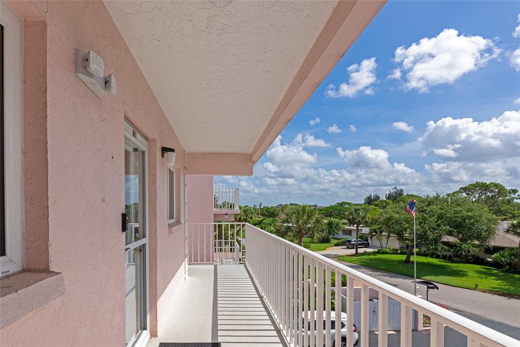 A pink exterior balcony features a white metal railing overlooking a street and green trees — 910 GOLDEN BEACH BOULEVARD UNIT 202, VENICE, FL