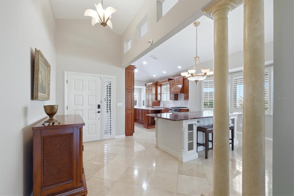 An entryway leads into a kitchen with a white island, wood cabinetry, and tile flooring — 7765 CALLE FACIL, SARASOTA, FL