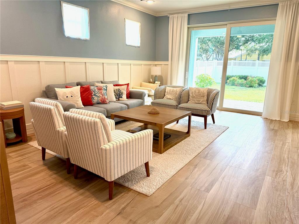 A living room features a gray sofa, striped armchairs, a wooden coffee table, and sliding doors — 319 SHORE CRAB WAY, APOLLO BEACH, FL