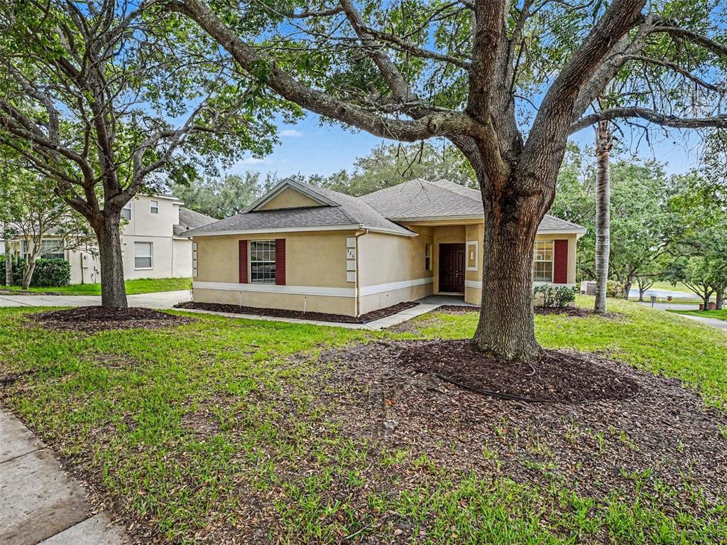 A single-story tan house with red shutters sits behind large trees on a grassy lot — 526 AZALEA BLOOM DRIVE, APOPKA, FL