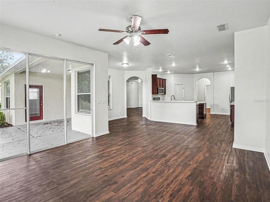 An open-concept living area features dark wood-look flooring, a ceiling fan, and sliding glass doors — 526 AZALEA BLOOM DRIVE, APOPKA, FL