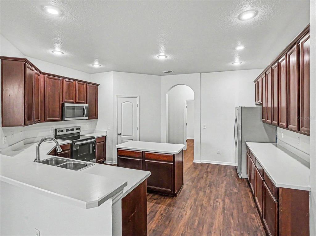 A kitchen features dark wood cabinets, white countertops, stainless steel appliances, and wood-look flooring — 526 AZALEA BLOOM DRIVE, APOPKA, FL