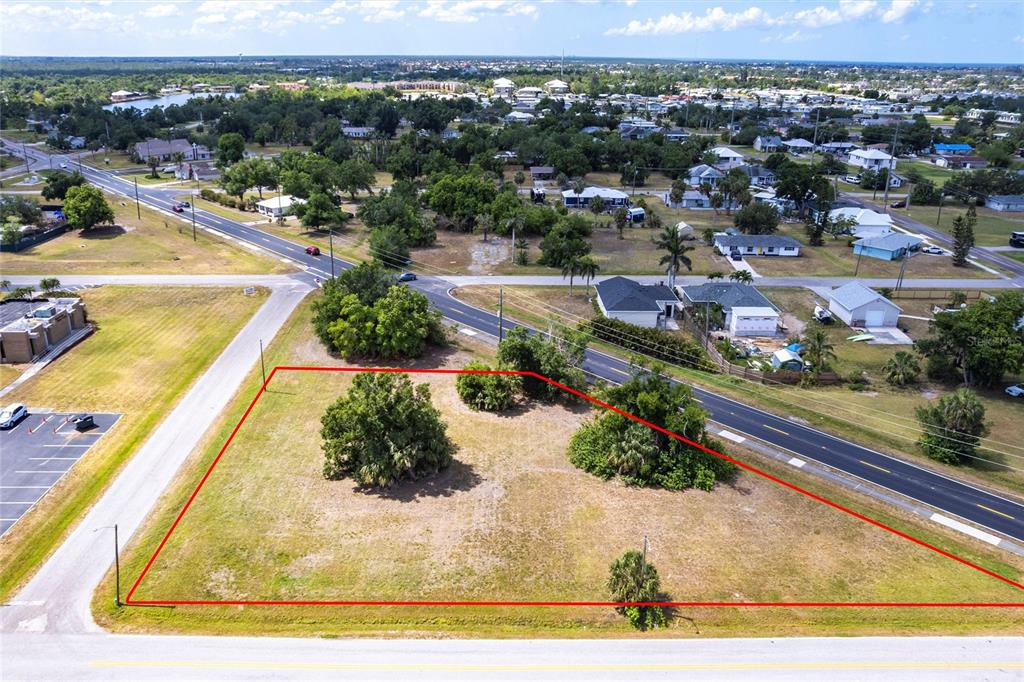 An aerial view shows a vacant, grassy corner lot outlined in red next to roads — 403 E ANN STREET, PUNTA GORDA, FL