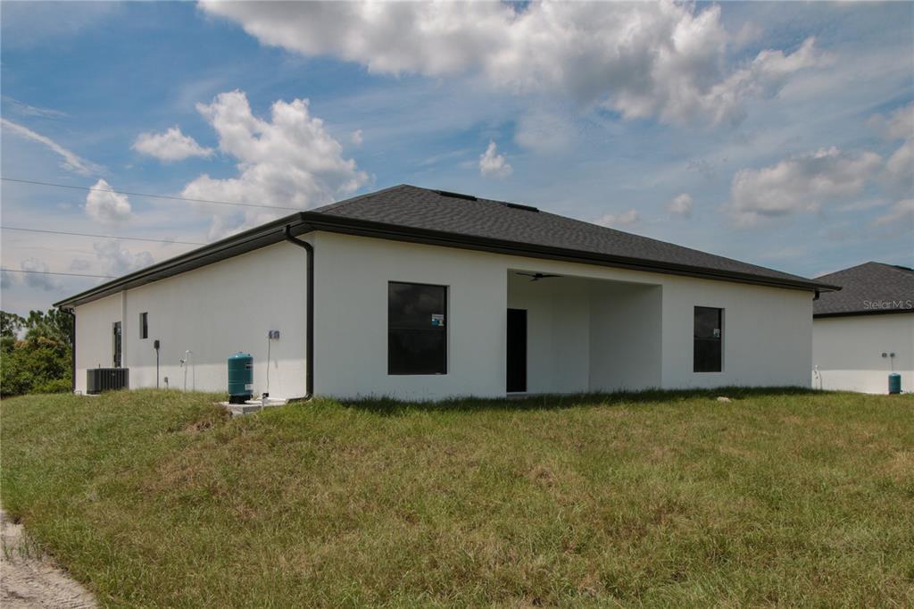 The rear exterior of a white, single-story house features a covered patio and dark trim — 945 COMMODORE STREET, LEHIGH ACRES, FL