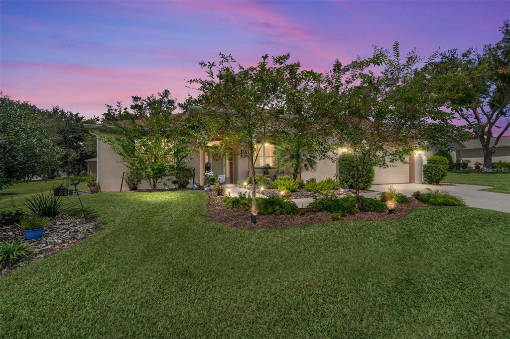 A single-story house with a landscaped front yard and a two-car garage at sunset — 13660 SE 90TH TERRACE, SUMMERFIELD, FL