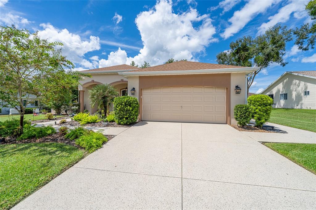 A tan single-story house with a two-car garage, a concrete driveway, and landscaped front yard — 13660 SE 90TH TERRACE, SUMMERFIELD, FL