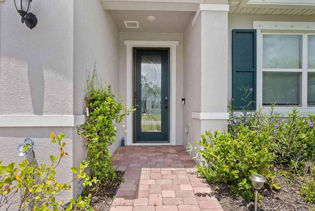 A paved walkway leads to a front entrance with a glass-paneled door and landscaping — 7322 34TH COURT E, SARASOTA, FL