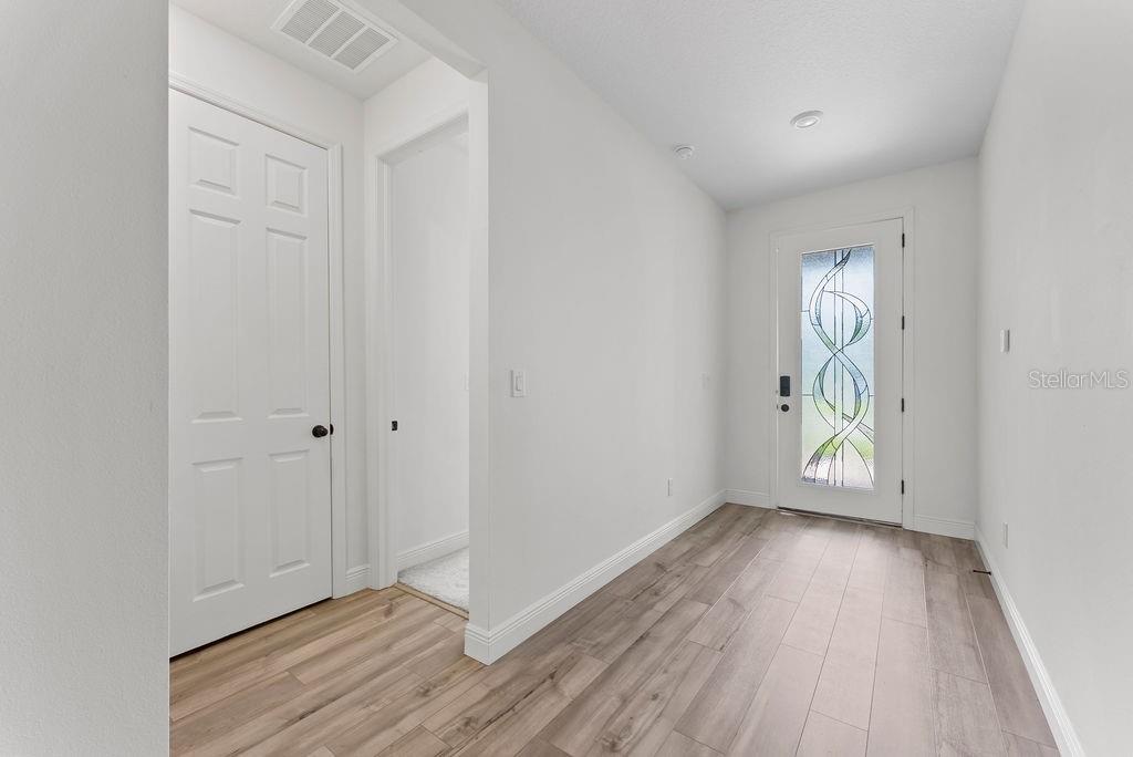 An entryway features light wood-look flooring, white walls, a white door, and a decorative glass insert — 7322 34TH COURT E, SARASOTA, FL