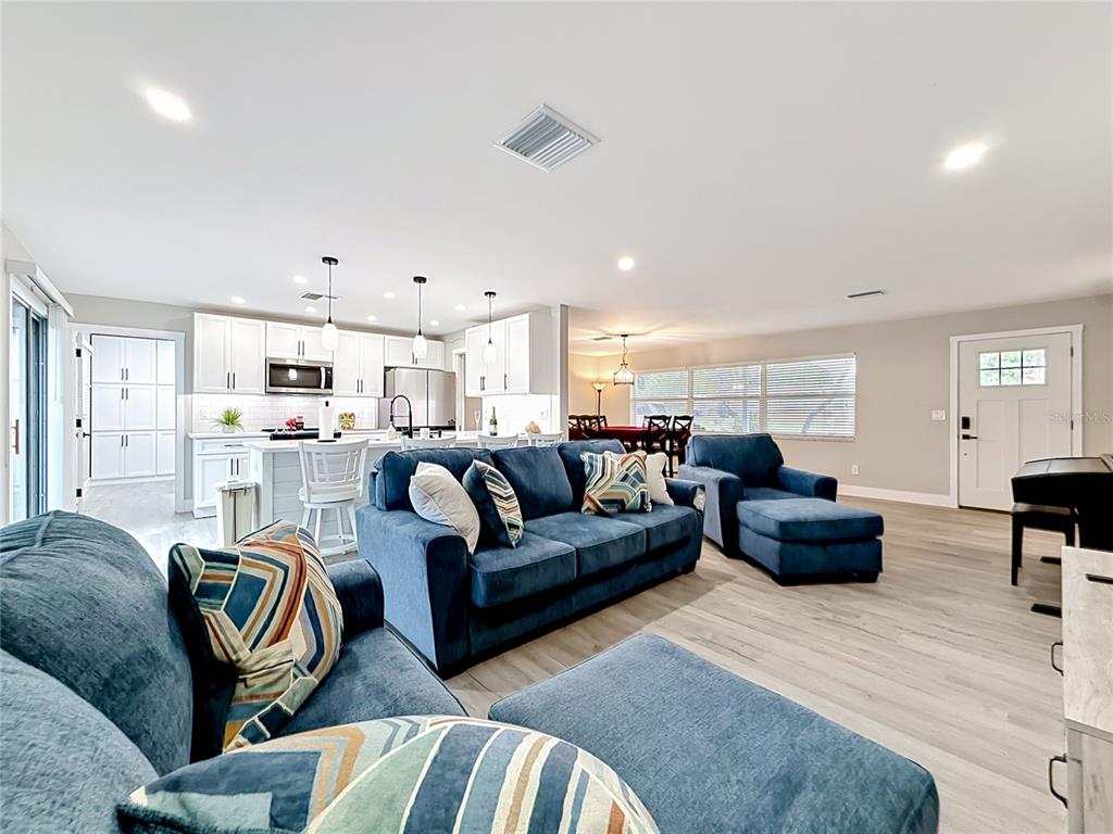 An open-concept living room and kitchen feature blue sofas, white cabinetry, and light wood flooring — 508 SHORE DRIVE, LARGO, FL