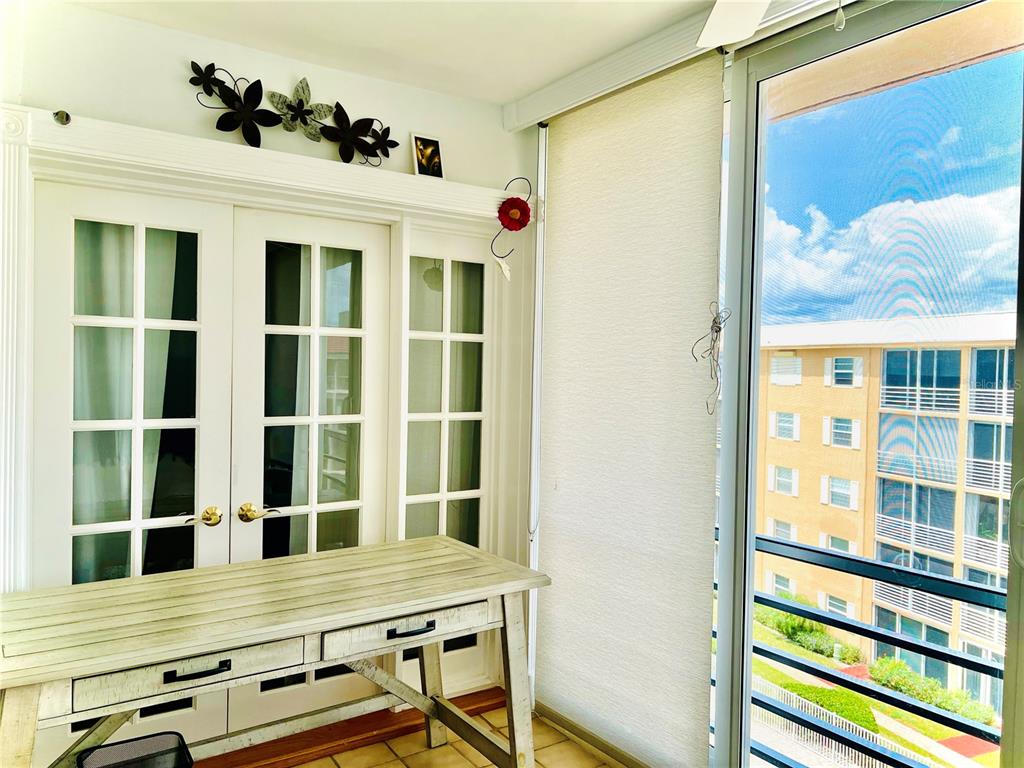 A sunroom features a white desk, French doors, and a view of an adjacent apartment building — 304 GOLFVIEW ROAD UNIT PH, NORTH PALM BEACH, FL