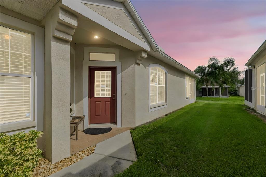 A side view of a beige house exterior featuring a red door and a grassy yard — 11435 CAMBRAY CREEK LOOP, RIVERVIEW, FL