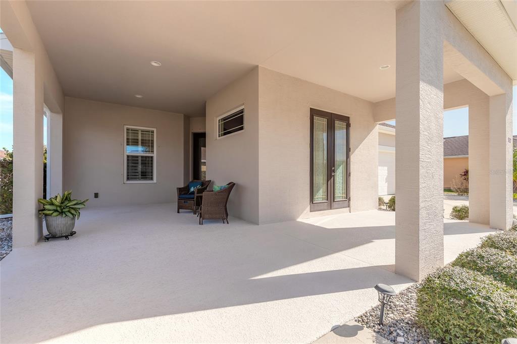 A covered patio features a concrete floor, two wicker chairs, and a potted plant — 527 LUNA BELLA LANE, NEW SMYRNA BEACH, FL