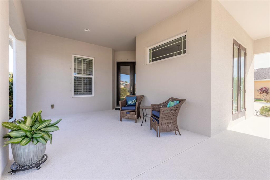 A covered patio features a light-colored floor, two wicker chairs, and a potted plant — 527 LUNA BELLA LANE, NEW SMYRNA BEACH, FL