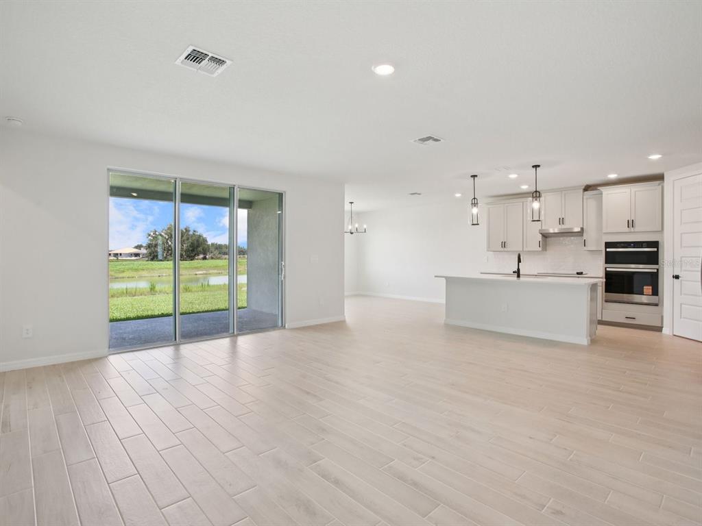 An open-concept kitchen and living area with light wood-look tile flooring and sliding glass doors — 11437 STARLING SONG PLACE, PARRISH, FL