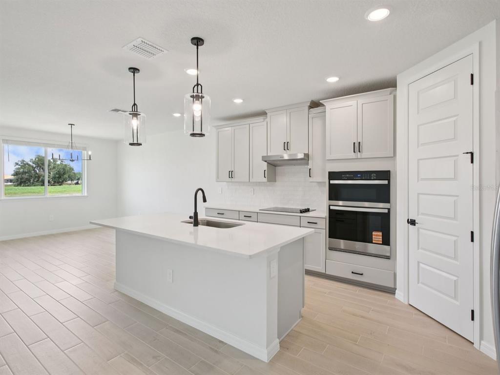 A modern kitchen features a white island, light gray cabinetry, stainless steel appliances, and tile flooring — 11437 STARLING SONG PLACE, PARRISH, FL